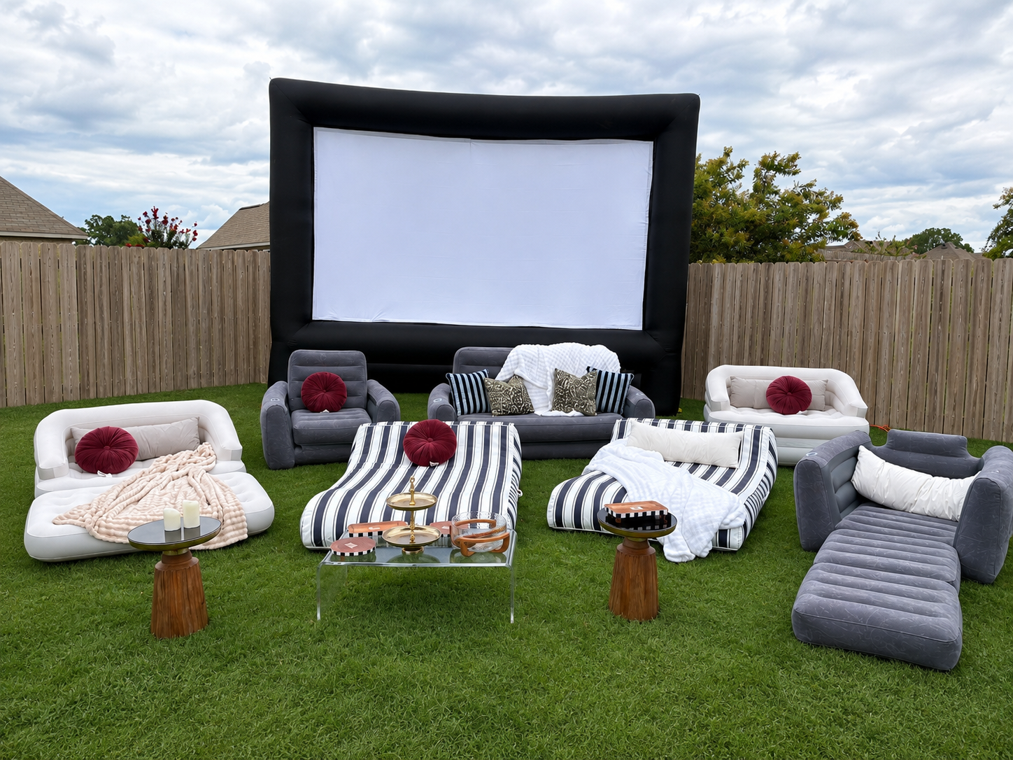 Velvet Ditch backyard setup with a large inflatable screen, white and grey inflatable couches, striped loungers, and side tables on the lawn